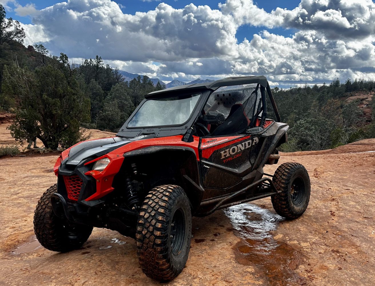 Vibrant red rock formations under a blue sky, winding dirt trails cutting through a rugged landscape, scattered desert vegetation, adventurous off-road vehicles traversing challenging terrain, dramatic shadows cast by towering cliffs, panoramic views of Sedona's natural beauty.