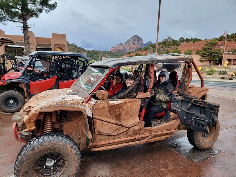 Vivid red rock formations under a bright blue sky, rugged UTVs parked on a dirt trail, surrounded by lush desert vegetation, panoramic views of scenic landscapes, adventurous atmosphere with dust trails in the air.