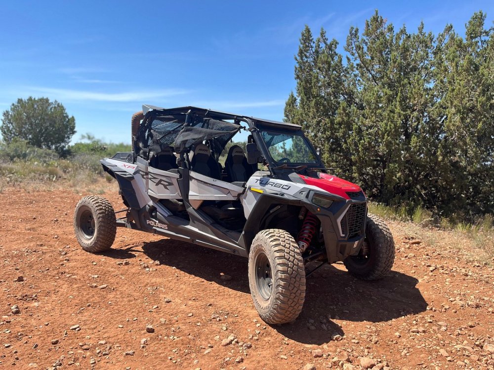 Vibrant desert landscape in Sedona, Arizona, showcasing red rock formations under a clear blue sky, with rugged UTVs navigating through sandy trails and rocky paths, dust clouds swirling behind, surrounded by lush green vegetation and distant mountains, capturing the thrill of off-road adventure.